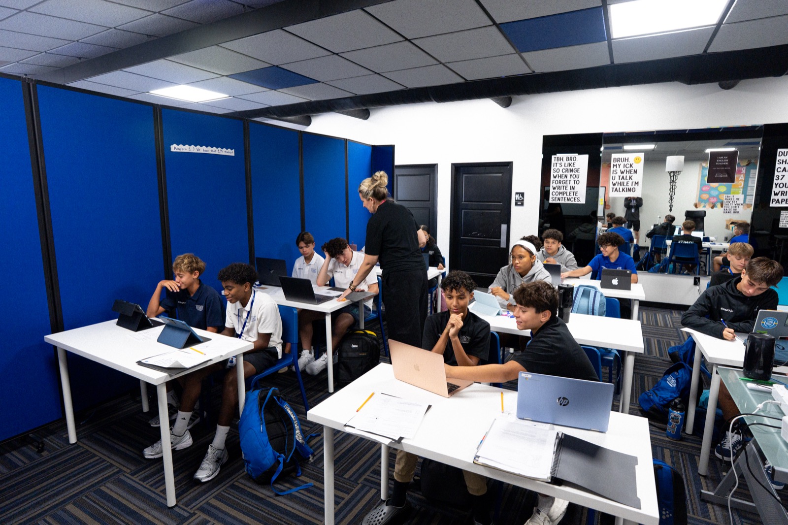 Teacher assisting student in modern classroom with laptops and tablets