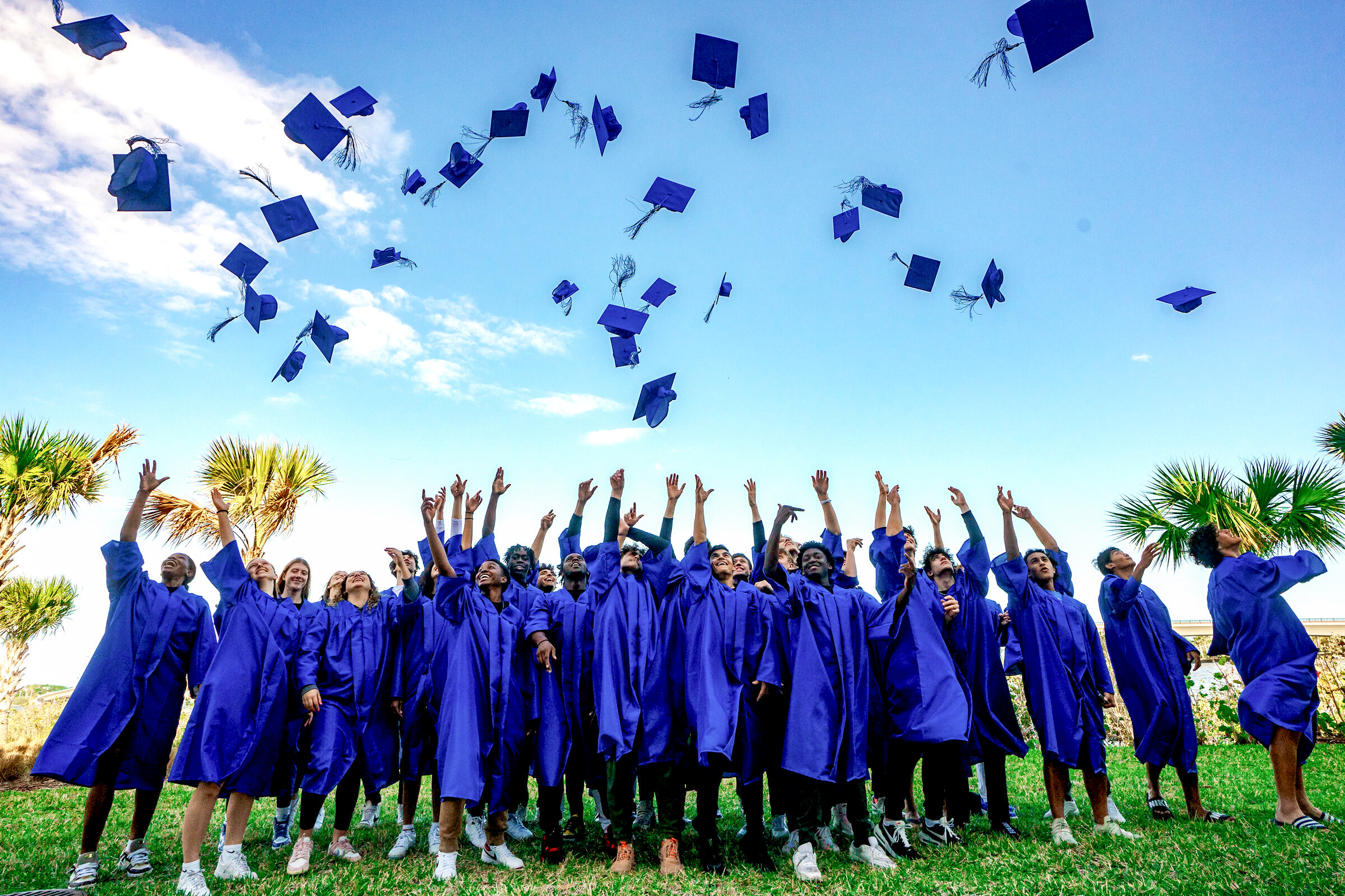 DME Academy graduates tossing caps in blue robes with palm trees