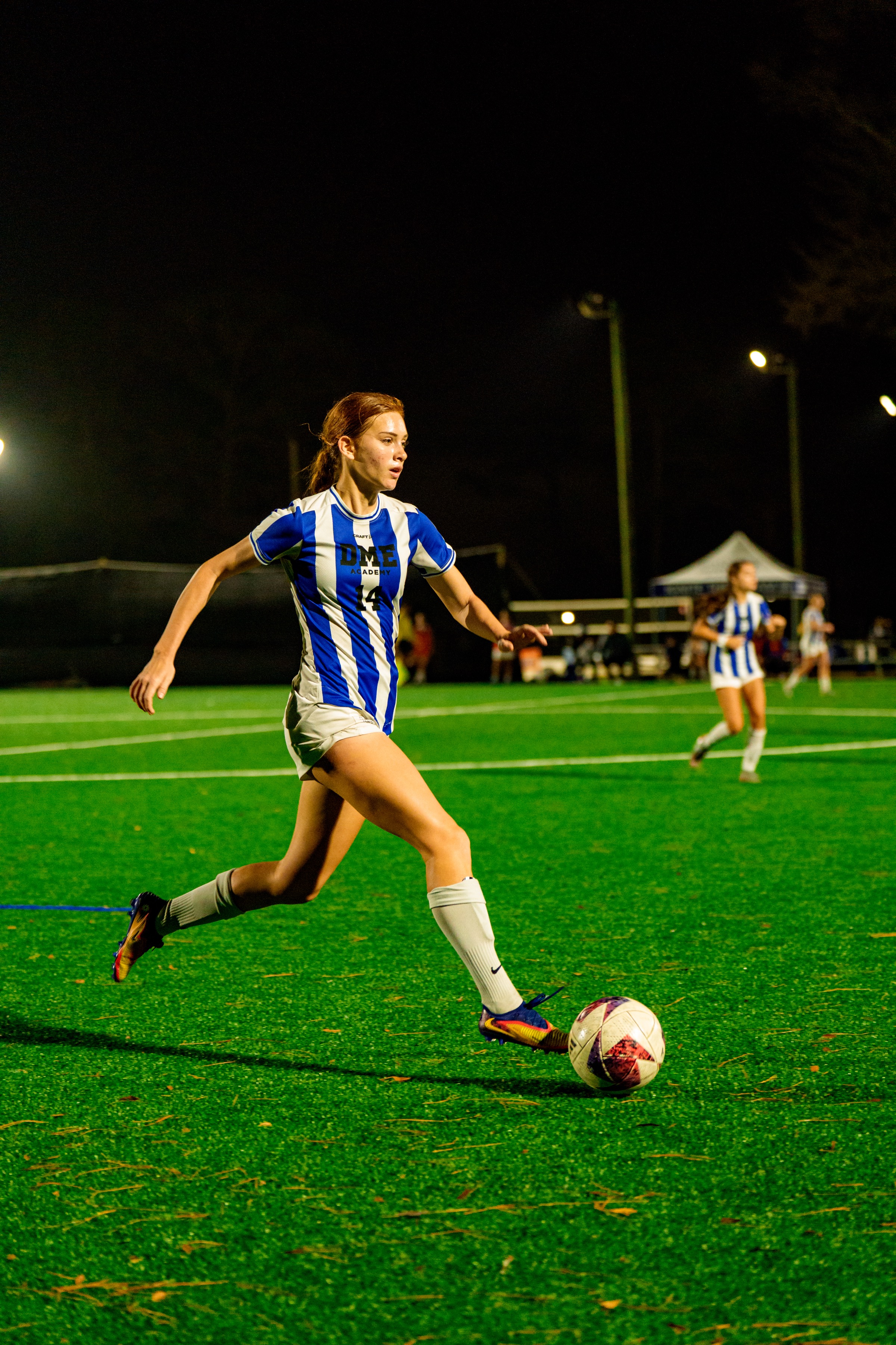 Female soccer player dribbling during night game under stadium lights